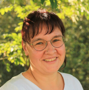 Porträt von einer Frau in weißem Shirt mit braunen Haaren und einer Brille.